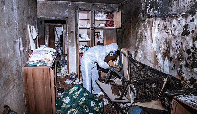 Expert in protective gear cleaning a fire-damaged room with charred walls and scattered debris