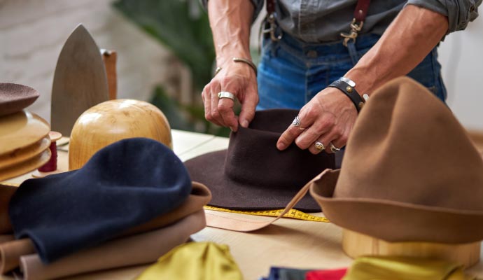 A professional restoring various types of hats and clothing items