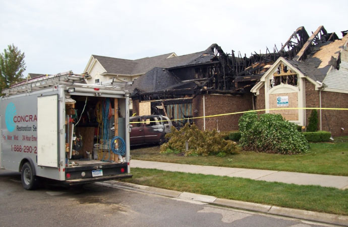 A fire damaged home with a Concraft restoration service vehicle parked in front
