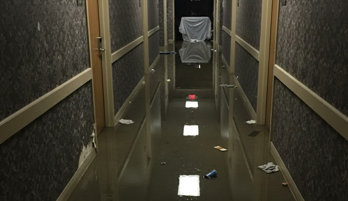 Flooded hallway with standing water debris and indoor storm damage inside residential or commercial property