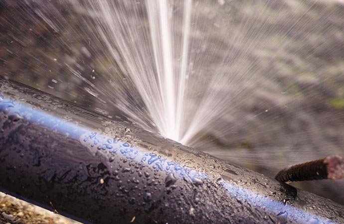 A black pipe with a leak where water is spraying out forcefully