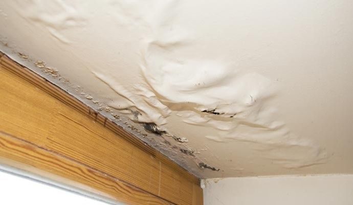 Ceiling with water damage showing bubbling paint and discolored areas caused by a roof leak