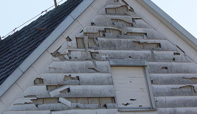 House siding damaged by hail, showing dents and broken exterior surfaces